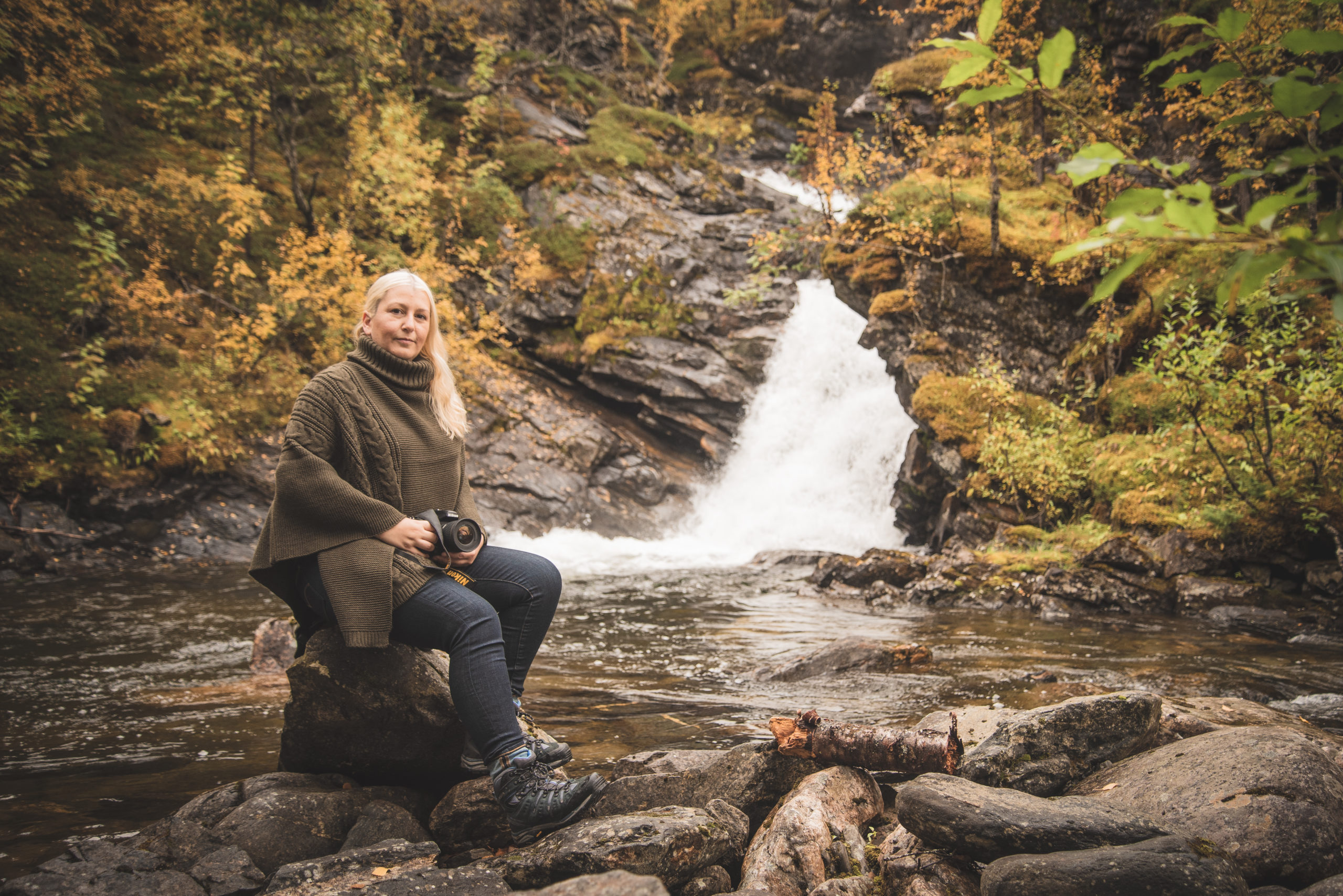 Female sitting relaxing on rocks near a waterfall in autumn.
