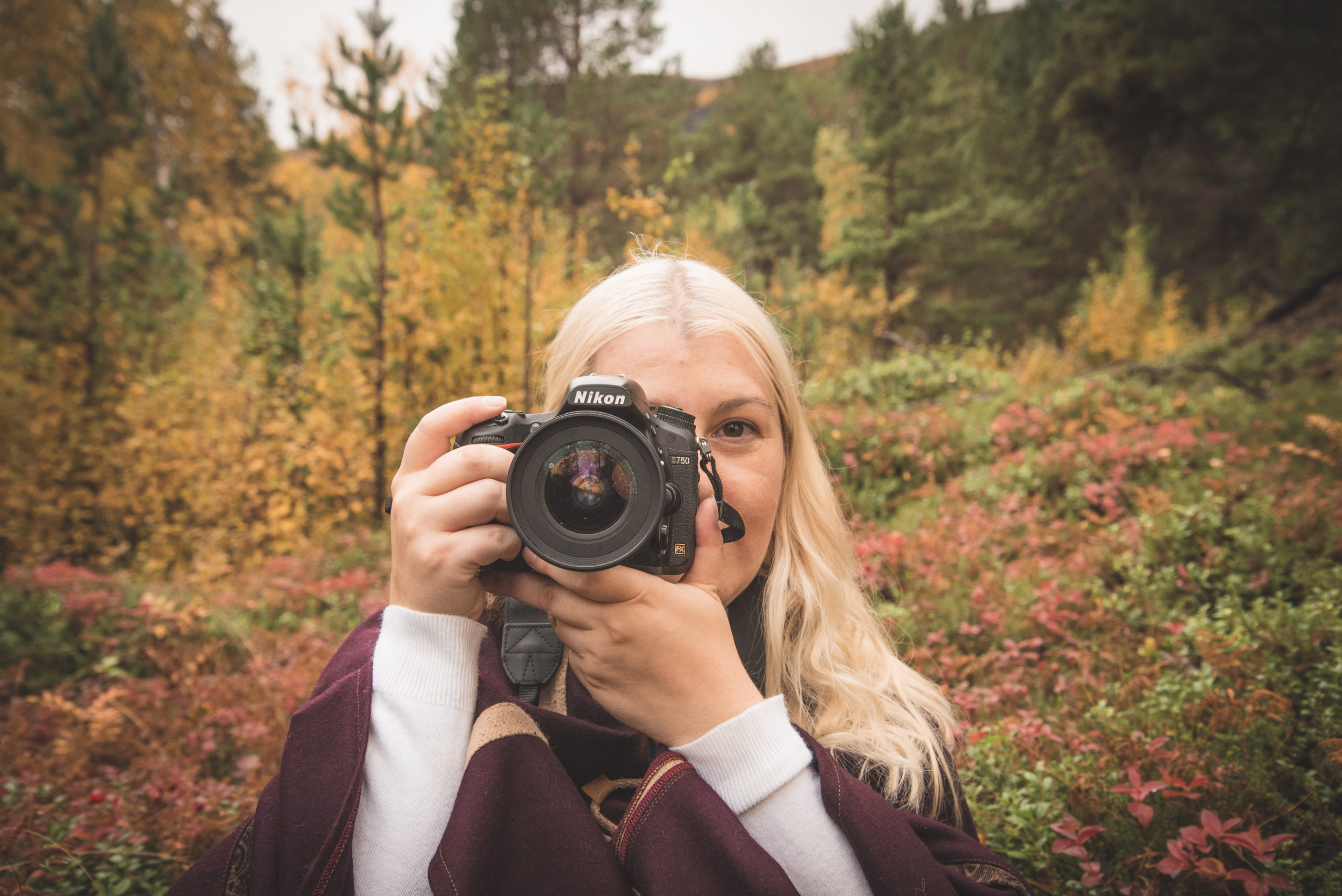 female photographer looking down camera lens with autumn forest background